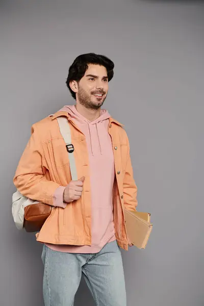 Ein junger Mann in orangefarbener Jacke und rosa Kapuzenpulli geht selbstbewusst mit Büchern um und versprüht Charme. — Stockfoto