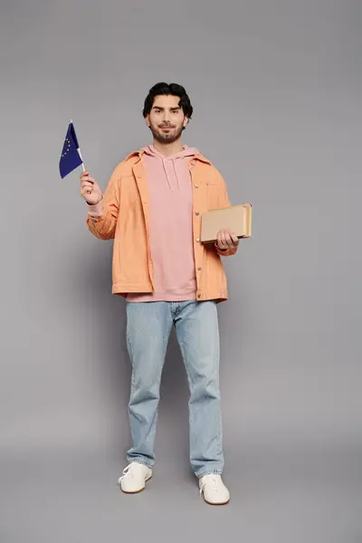 A young man with dark hair holds a flag and notebook, celebrating creativity indoors. — Stock Photo
