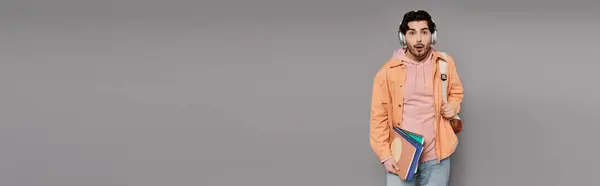 A young handsome man stands confidently against a gray backdrop, wearing a trendy jacket. — Stock Photo