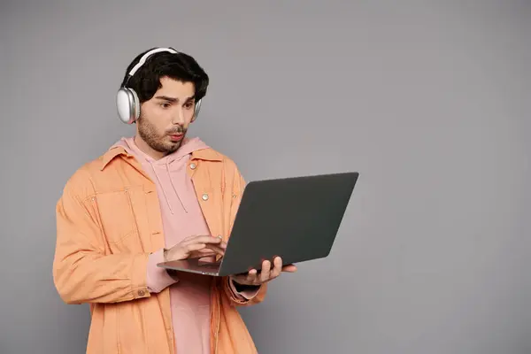 Um jovem bonito usando fones de ouvido se envolve com seu laptop, mostrando concentração e estilo. — Fotografia de Stock