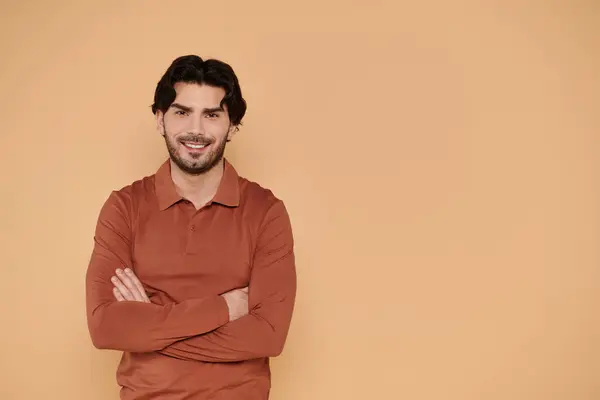 A stylish young man stands with crossed arms, smiling warmly in a cozy atmosphere. — Stock Photo