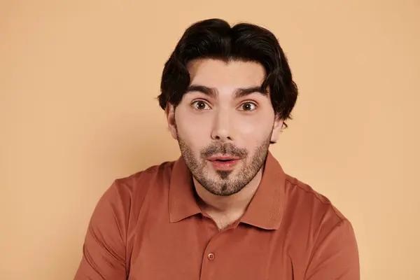 Un hombre joven y guapo con el pelo moreno muestra una expresión de sorpresa, sentado casualmente. - foto de stock