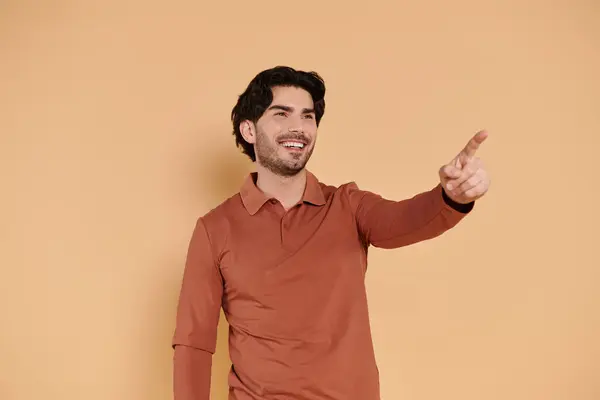 A young brunette man in a stylish orange shirt smiles and gestures with excitement. — Stock Photo