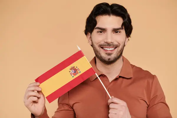 A young handsome man beams with pride as he holds a Spanish flag against a warm backdrop. — Stock Photo