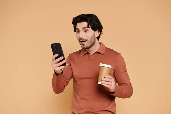 A young man with dark hair smiles brightly as he checks his phone while enjoying coffee. — Stock Photo