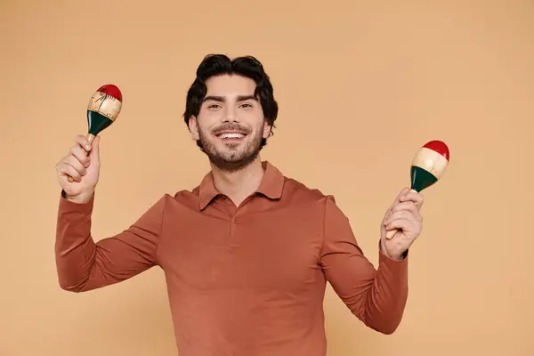 Ambiente brillante creado como un joven guapo juega a las maracas con una sonrisa alegre. - foto de stock