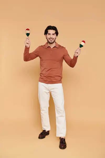 Smiling young man enjoys playing maracas with energy and enthusiasm, dressed in casual attire. — Stock Photo