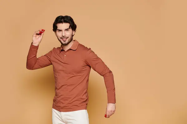 A young, charming brunette man in a rust colored top joyfully engages with colorful items, smiling. — Stock Photo