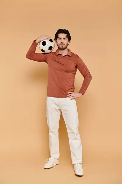 A young man balances a soccer ball on his head, radiating confidence in a bright studio. — Stock Photo