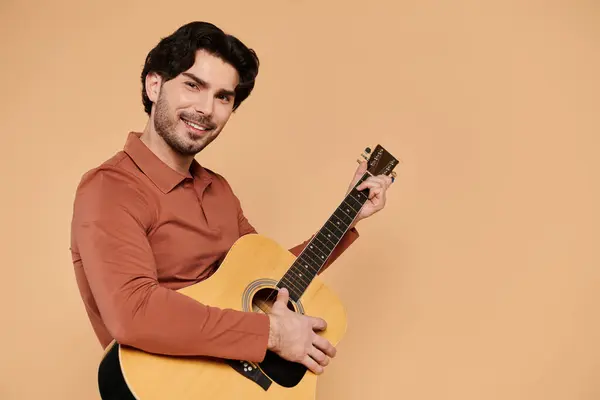 Brunette man engages in music, smiling brightly while strumming his guitar in a vibrant setting. — Stock Photo
