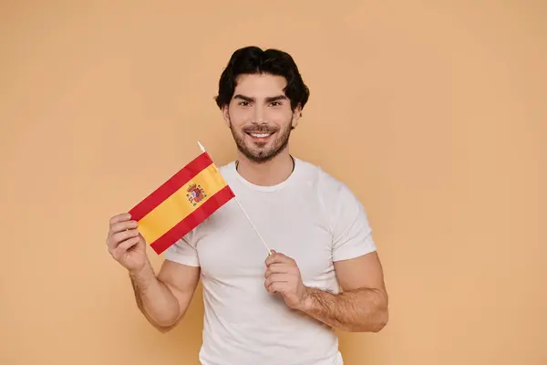 Bello giovane uomo sorride mentre mostra una piccola bandiera spagnola, irradiando gioia e orgoglio. — Foto stock