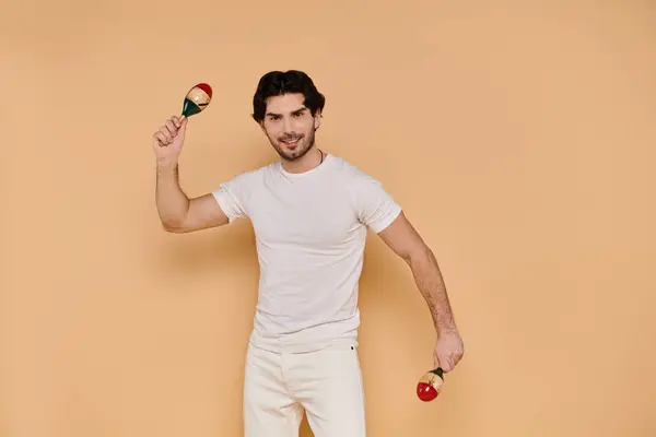 A young handsome man joyfully plays maracas while smiling brightly, immersed in music. — Stock Photo