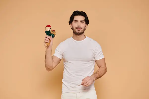 A young handsome man with brunette hair is happily shaking maracas in a light studio. — Stock Photo