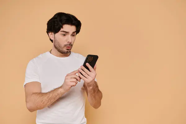 Handsome young man with brunette hair engages with his smartphone, surprised by content. — Stock Photo