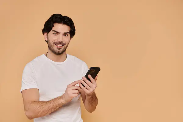 Un bel giovane uomo si impegna con il suo smartphone, trasudando fascino e positività in un ambiente accogliente. — Foto stock