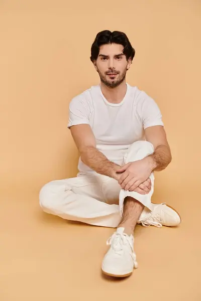 A young man sits relaxed on the floor with a gentle smile, dressed in casual white apparel. — Stock Photo