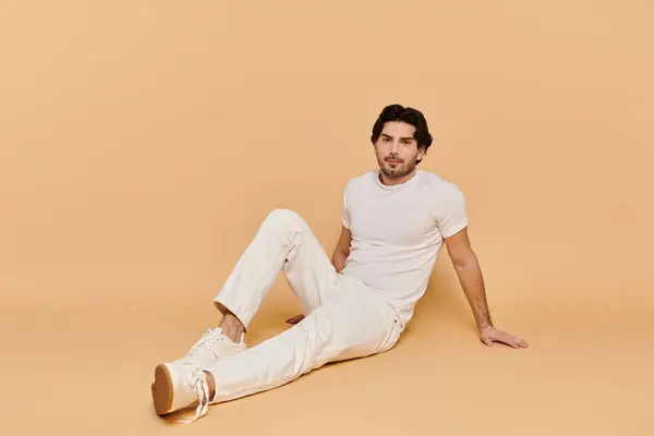 A young man with brunette hair relaxes against a warm yellow backdrop in casual style. — Stock Photo