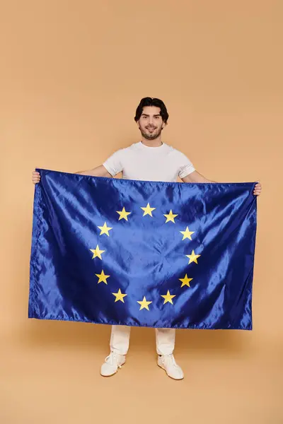 Ein junger gutaussehender Mann steht stolz und zeigt eine lebendige europäische Flagge, die Zuversicht ausstrahlt.. — Stockfoto