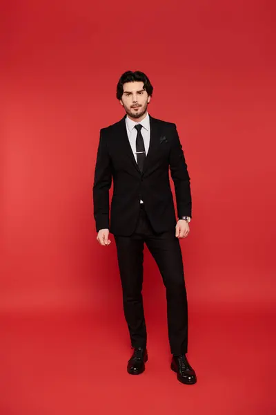 A young handsome man stands tall in a polished black suit, exuding confidence and charm. — Stock Photo