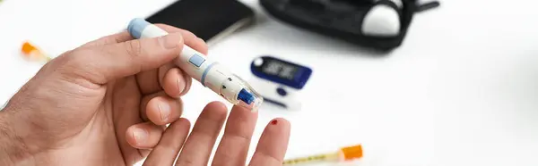 A young man with diabetes checks his blood sugar in a stylish home, demonstrating his daily routine, banner — Stock Photo