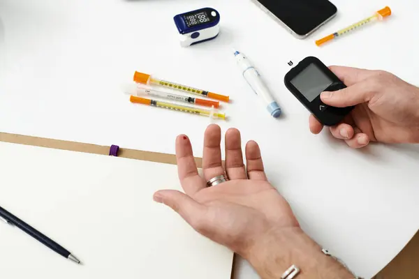 Giovane uomo controlla lo zucchero nel sangue con un metro mentre circondato da strumenti di gestione del diabete a casa. — Foto stock