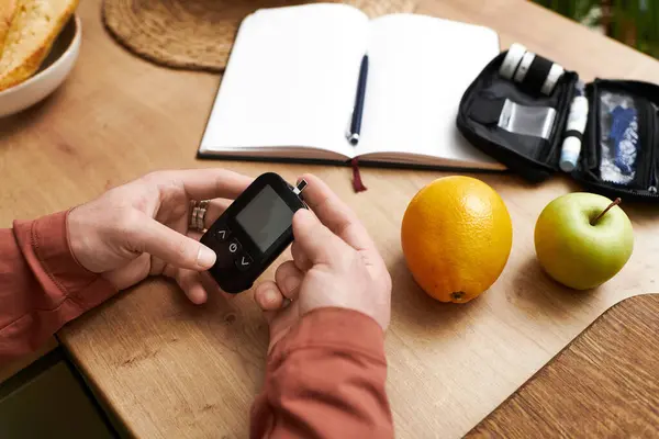 A young man checks his blood sugar levels at home surrounded by healthy snacks and planning tools. — Stock Photo
