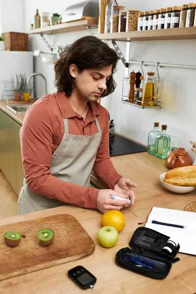 Ein junger Mann überprüft seinen Blutzuckerspiegel, während er zu Hause Obstsnacks zubereitet. — Stockfoto