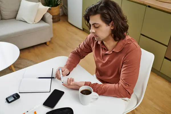 Man checks his blood sugar and manages his diabetes routine while enjoying coffee at home. — Stock Photo