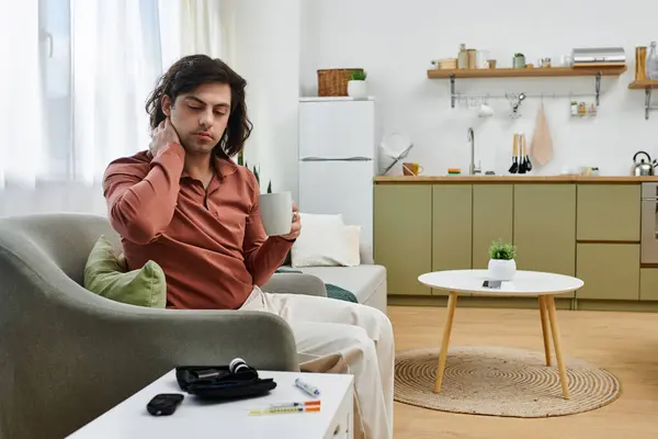 A young man with diabetes is relaxing at home, monitoring his health while enjoying a drink. — Stock Photo