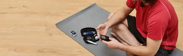 A young man checks his blood sugar on the floor, surrounded by diabetes supplies, banner — Stock Photo