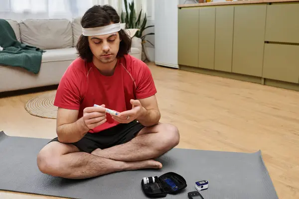 A young man practices self-care at home, checking his blood sugar levels while sitting comfortably. — Stock Photo