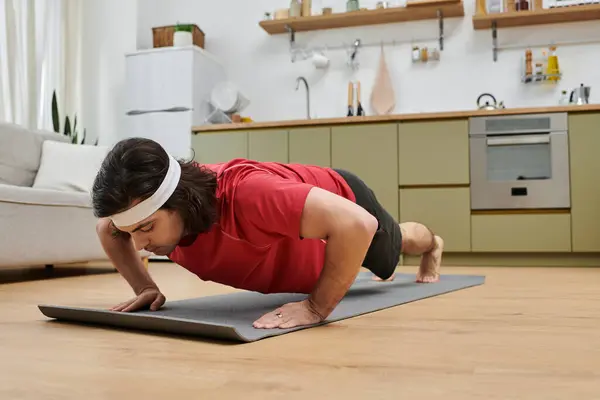 Joven se dedica a una rutina de ejercicios en una alfombra de fitness en su elegante apartamento. - foto de stock
