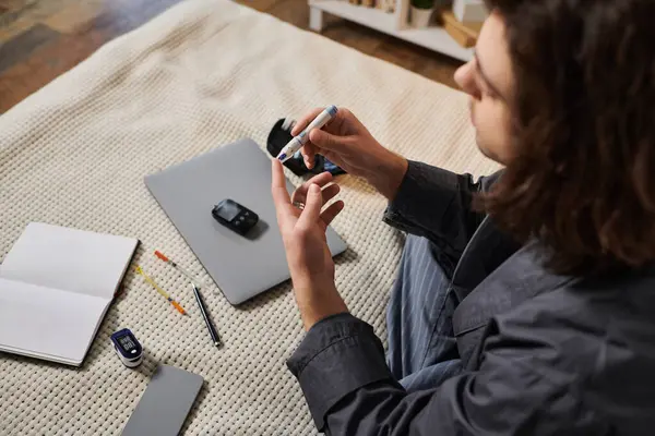 A young man with long hair monitors his blood sugar in a cozy home environment. — Stock Photo