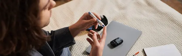 A young man checks his blood sugar while sitting in his stylish apartment, focusing on health, banner — Stock Photo