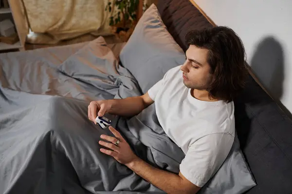 Young man relaxes in bed while managing diabetes and monitoring his health routine at home. — Stock Photo