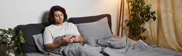 Caucasian man with long hair checks his device while relaxing in his cozy bed, managing diabetes, banner — Stock Photo