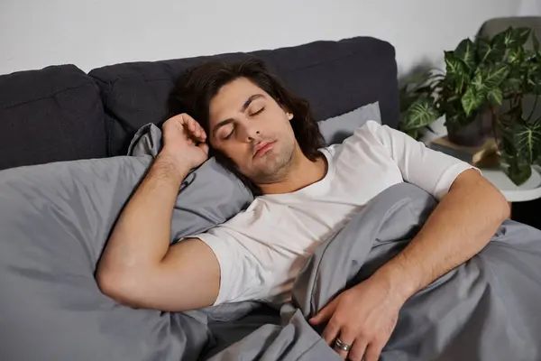 A good looking young man peacefully sleeps wrapped in cozy blankets in his stylish home. — Stock Photo