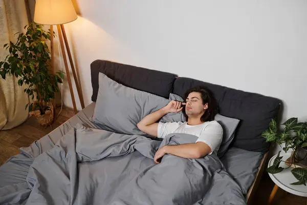 Un joven disfruta de un momento tranquilo en la cama, abrazando la comodidad en su elegante apartamento. — Stock Photo