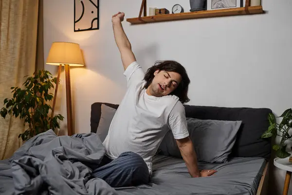 Joven se estira en la cama, abrazando la tranquila luz de la mañana de su casa. - foto de stock