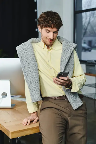 A young man dressed in a smart casual outfit relaxes while using his smartphone in the office. — Stock Photo