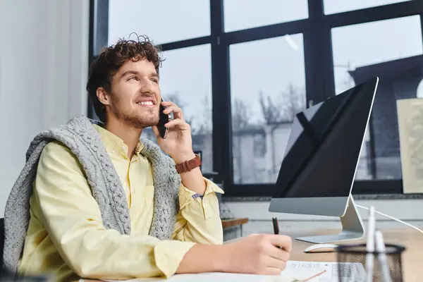 Young professional engages in a phone call while jotting notes at his stylish desk. — Stock Photo