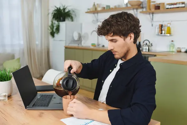 Curly-haired man in a stylish shirt pours coffee into a cup at home, immersed in work. — Stock Photo