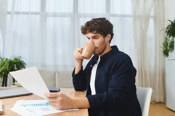 Handsome young man sips coffee and examines printed documents at home in a bright environment. — Stock Photo