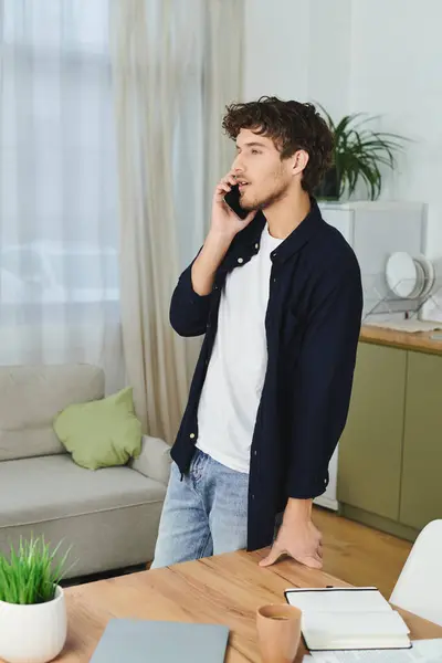 Curly-haired young man speaks on the phone while standing in his chic apartment, feeling at ease. — Stock Photo