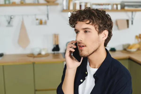 Beau jeune homme aux cheveux bouclés engagé dans une conversation téléphonique à l'intérieur à la maison. — Photo de stock