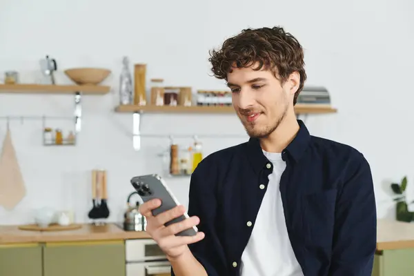 Uomo dai capelli ricci con una camicia elegante sorride mentre scorre il suo smartphone a casa. — Foto stock