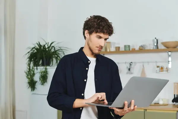 Curly-haired man focuses on his laptop while standing in a chic apartment setting. — Stock Photo