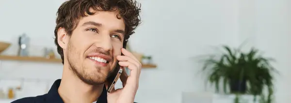 Un beau jeune homme aux cheveux bouclés profite d'une conversation téléphonique à la maison dans un cadre moderne, bannière — Photo de stock