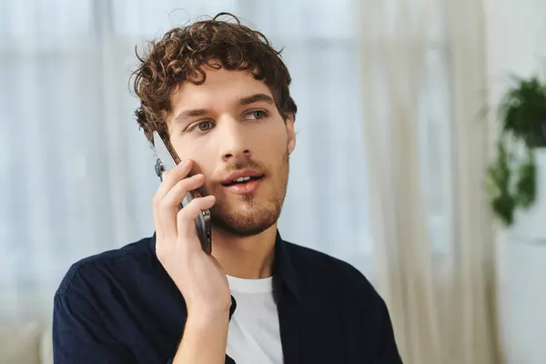 Bel homme avec les cheveux bouclés parle au téléphone dans son espace intérieur élégant, ambiance détendue. — Photo de stock