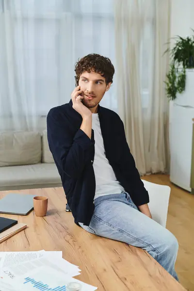 Young man with curly hair chats on the phone at his stylish dining table. — Stock Photo